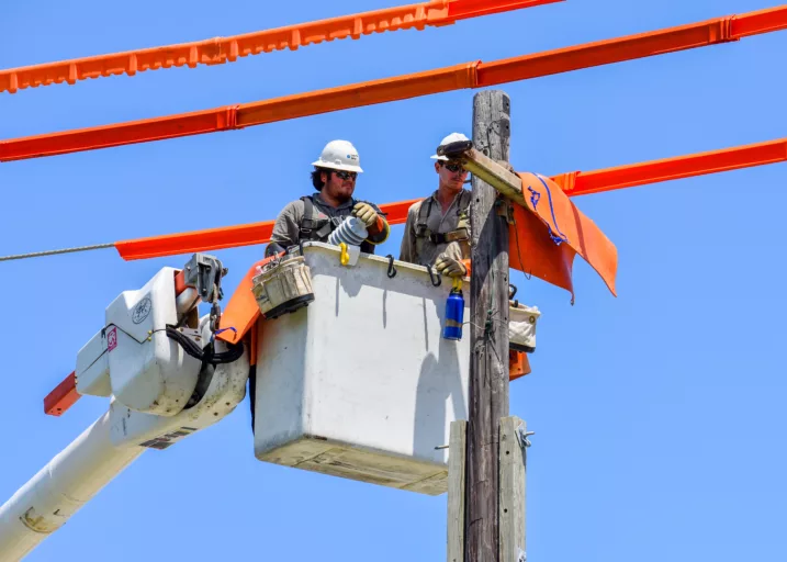 Two men with safety gear in a bucket truck working on an electrical pole