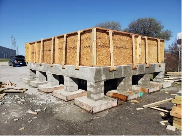 In a parking lot, a wooden frame is on top of a concrete slab with eight concrete pillars underneath.