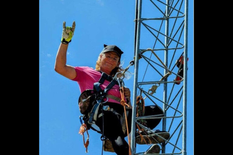 A woman in a pink shirt waving from a radio tower