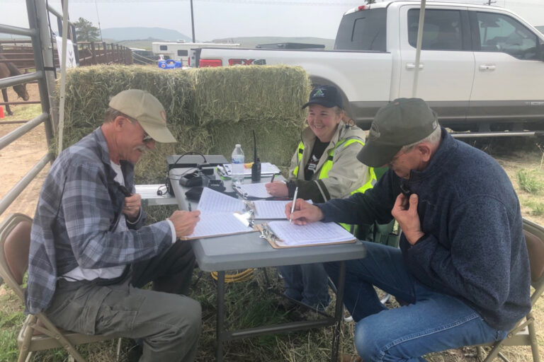 A woman and two men sitting at a table with radio equipment