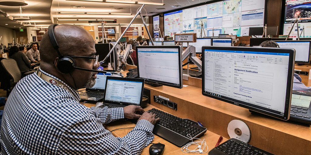 Man with headset sitting at a desk in front of computers