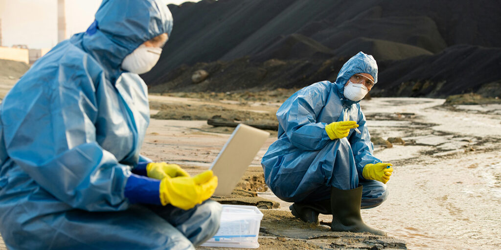 Two scientists in blue PPE gown and yellow gloves crouched while taking samples