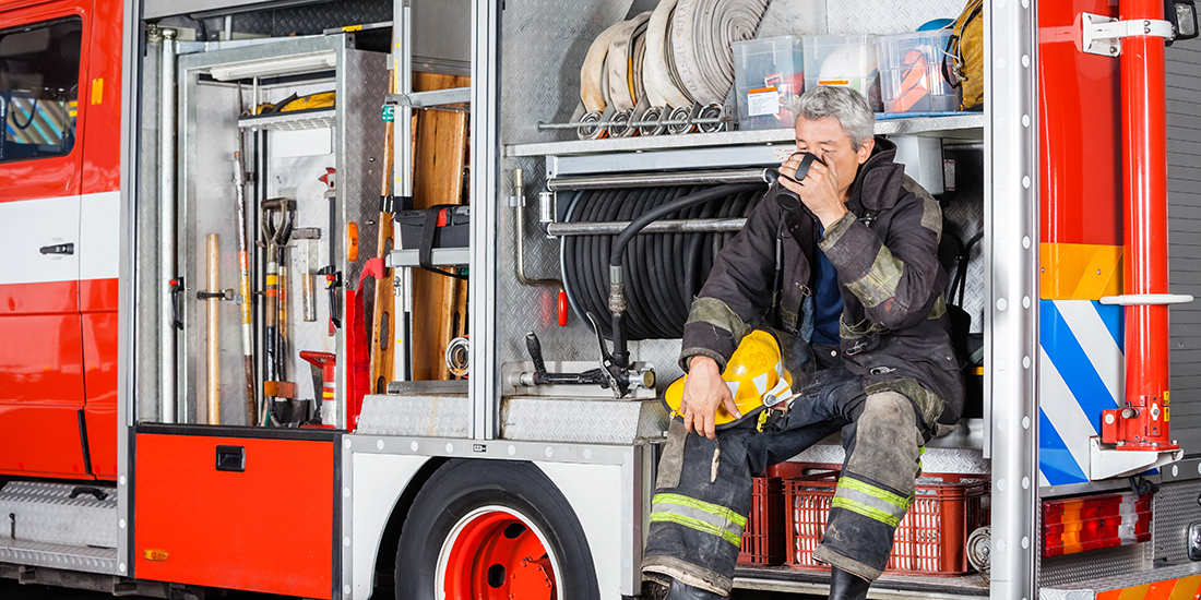 Full length of fireman drinking coffee while sitting in truck at fire station